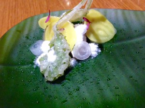 A leaf-shaped translucent plate with rings of white beets and turnips and whole leaves coated in tempura, hiding a slice of mackerel. The waiter then brings over what looks like a black river rock, opens it up and spoons out white beet snow that melts into dewdrops as it hits the plate.